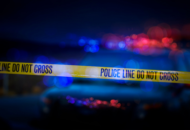 A photo illustration of police tape in front of blurry flashing police lights.