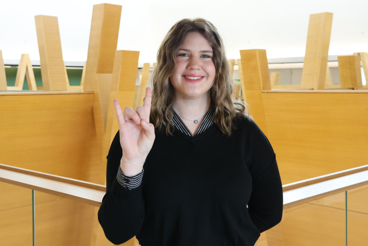 Ashley Parow stands in Honors College holding up Go Bulls hand sign