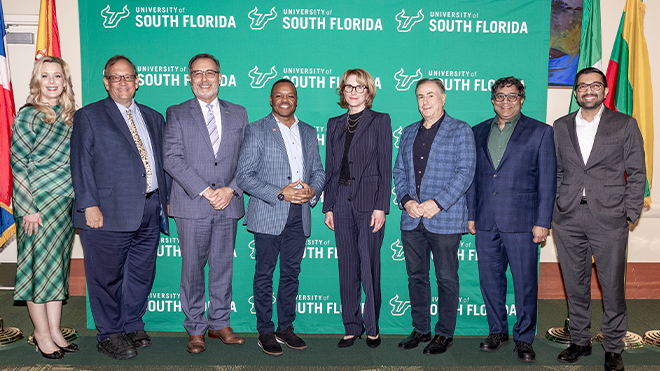 Panelists and speakers smiling in front of country flags and aoa体育 green backdrop