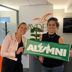 USF global alumnus Alexandre Garnier poses with Vanessa Martinez and an alumni sign during a visit to her Wayden office in Paris.